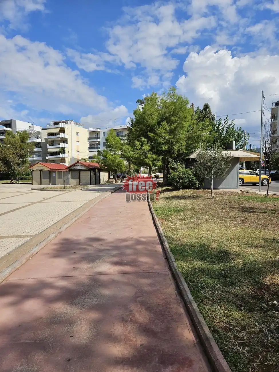 Άδειος πεζόδρομος στην πλατεία Παπανικολή στον Πειραιά με δέντρα και λίγα σύννεφα στον γαλάζιο ουρανό