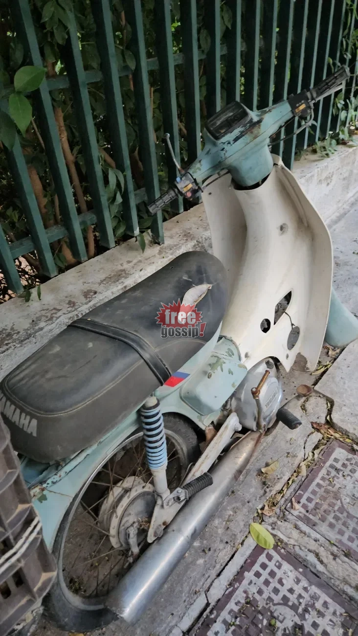 Παλιό γαλάζιο παπί Yamaha Townmate με φθαρμένη σέλα σταθμευμένο σε πεζοδρόμιο δίπλα σε κάγκελα